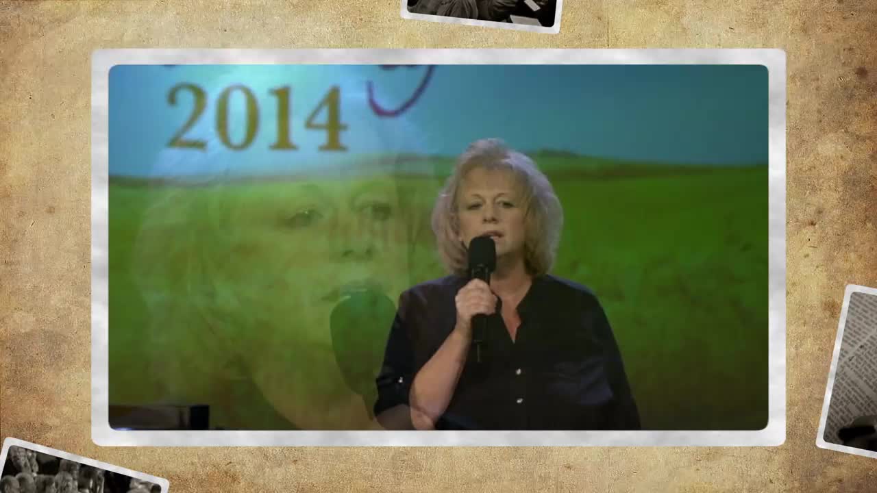 A woman stands at a podium, holding a microphone and speaking into it. Behind her, a screen displays "2014" and a faint image of another woman's face.