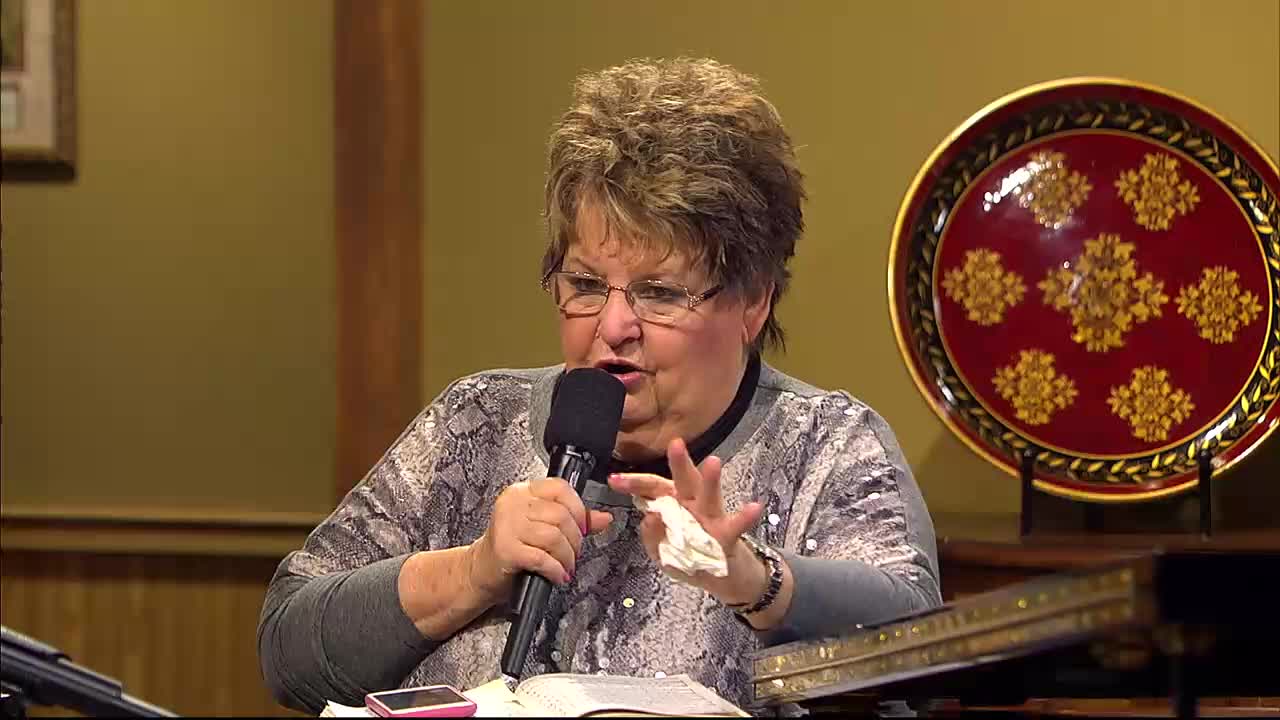 A woman speaks into a microphone, gesturing with her hands. She's on a program for the 3ABN Praise Him Music Network, likely in the United States.