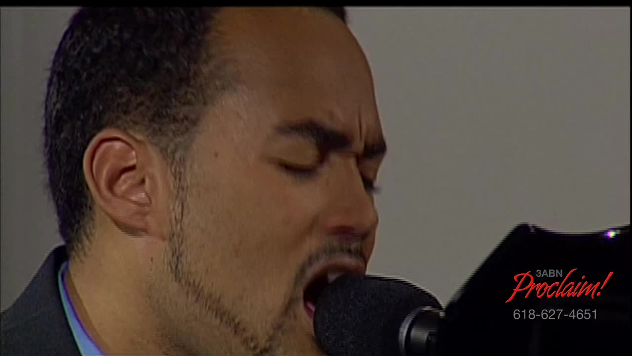 A man, his eyes closed, sings into a microphone with his mouth wide open. The 3ABN Proclaim! logo is visible in the corner, and the man seems to be on a television broadcast.
