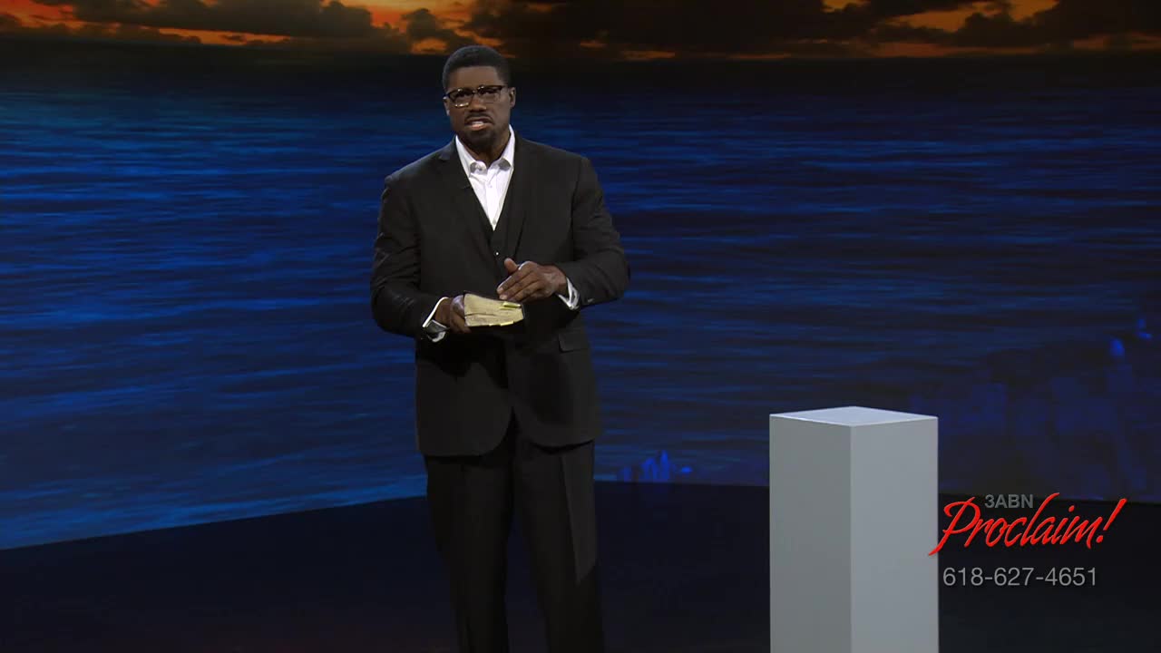 A man in a suit stands on a stage, holding a book. The 3ABN Proclaim! Network logo is visible in the corner.
