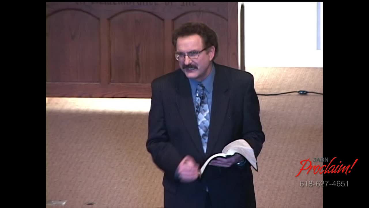 A man in a dark suit and glasses stands holding a book, speaking into the camera. The 3ABN Proclaim! logo is visible in the corner.
