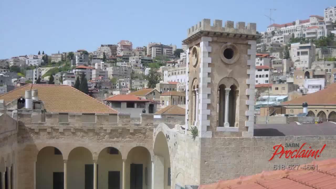 The 3ABN Proclaim! Network logo is in the corner of a stone building with a tower. Beyond the structure, a hillside town sprawls under a bright sky.
