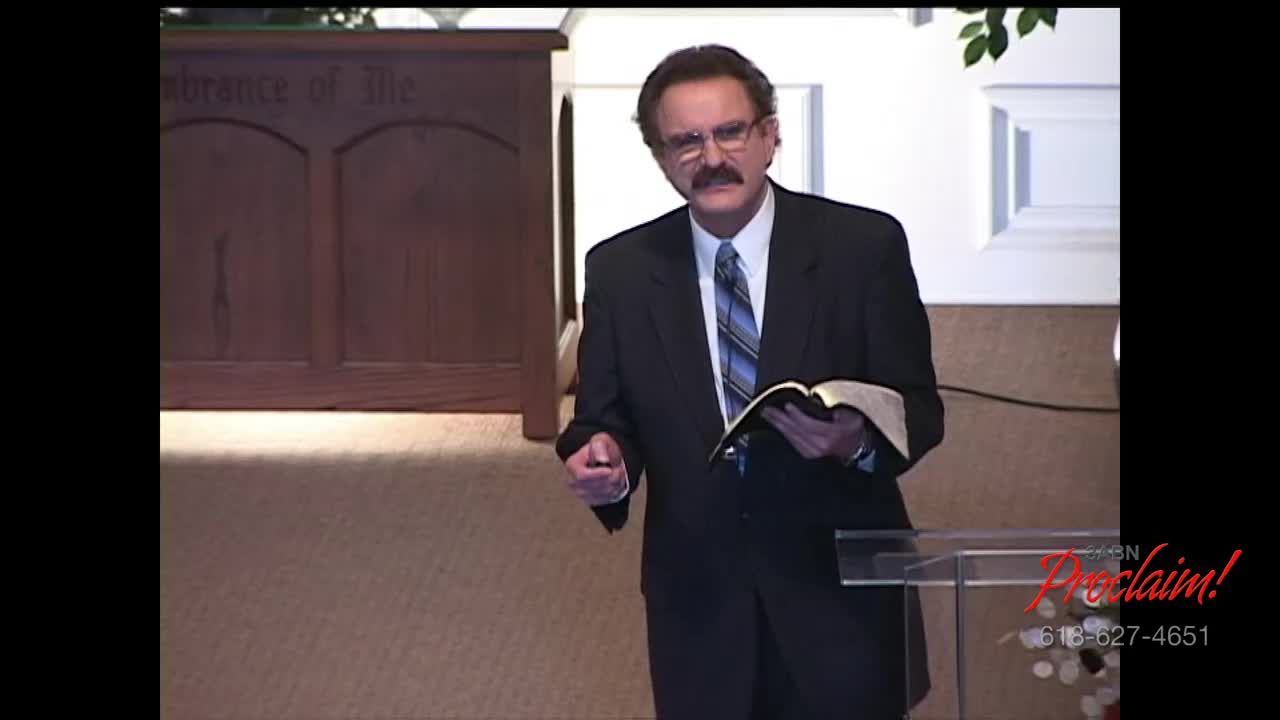 A man in a suit stands at a podium, holding an open book. He gestures with one hand as he speaks on the 3ABN Proclaim! Network from the United States.
