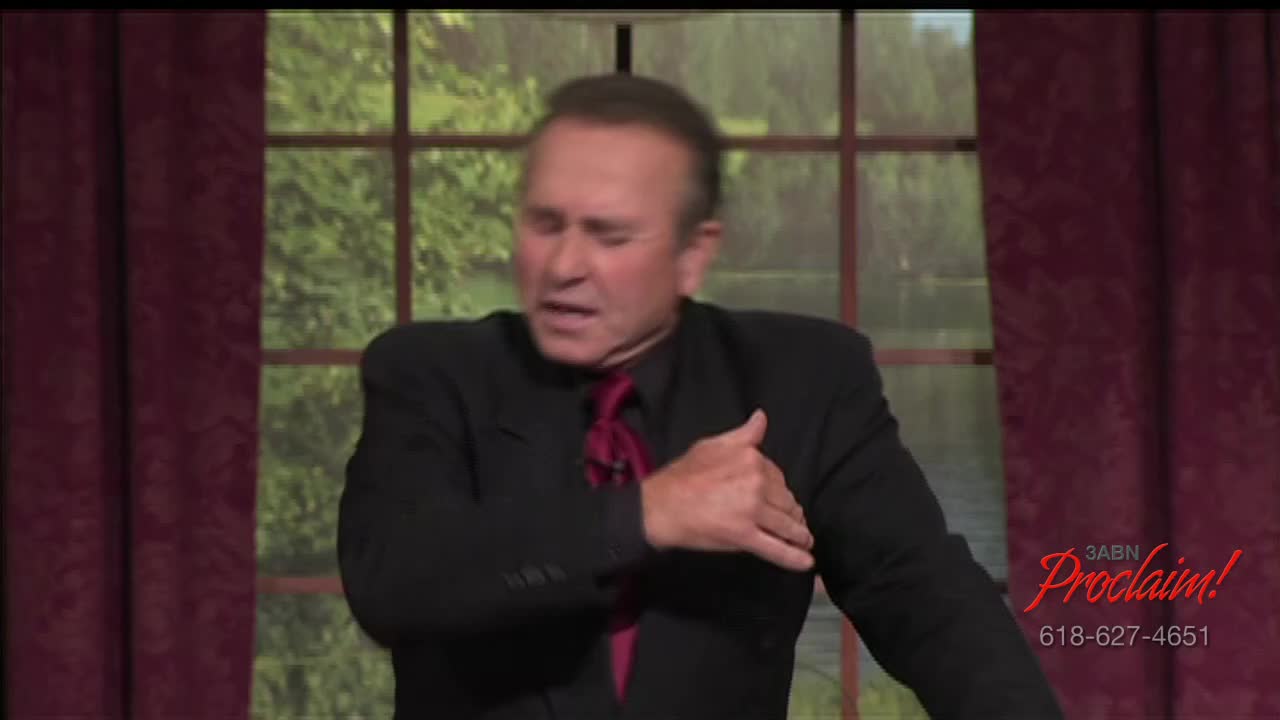 The man in the black suit gestures with his right hand toward his chest. He's on the set of a 3ABN Proclaim! broadcast.
