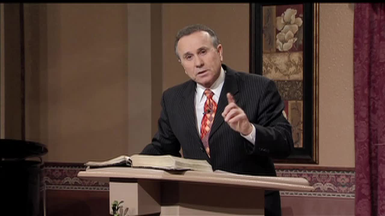 A man in a suit gestures emphatically, speaking from behind a lectern in what appears to be a studio. He's on the 3ABN Proclaim! Network in the United States, with a Bible open in front of him.
