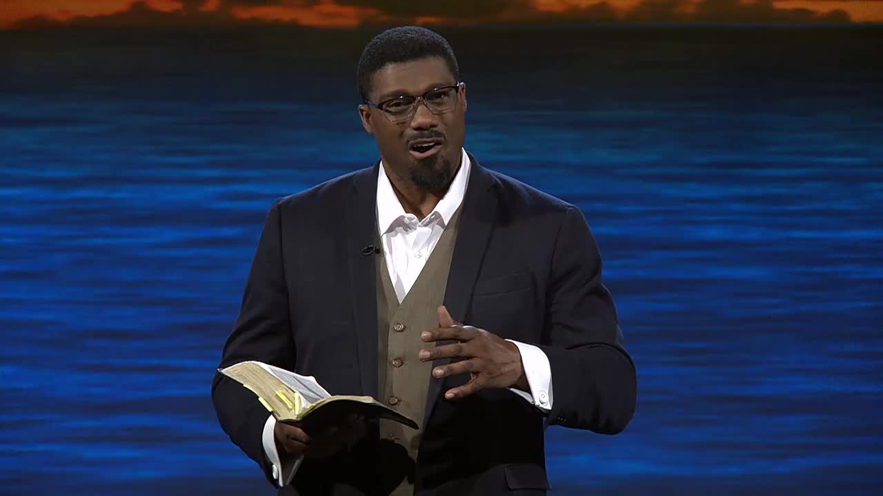 A man in a suit and glasses holds an open Bible, gesturing with his right hand. He is speaking, likely on the 3ABN Proclaim! Network.
