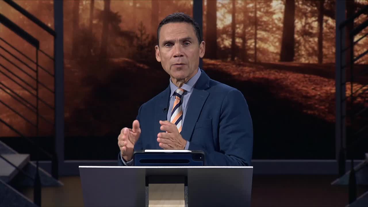 A man in a blue suit gestures with his hands while speaking from behind a podium. The background is a blurred image of a forest, likely for a broadcast on the 3ABN Proclaim! Network in the United States.
