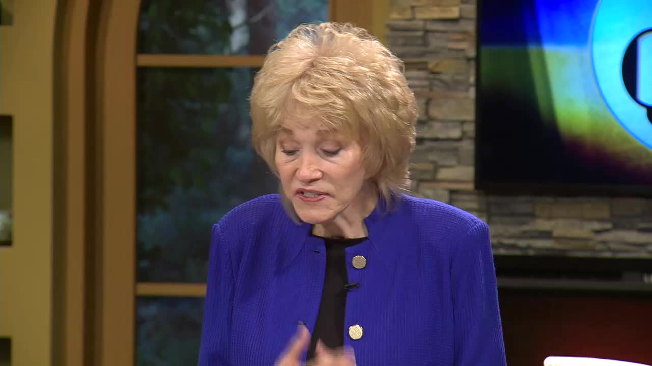 A woman in a blue blazer gestures with her hands as she speaks on the 3ABN Proclaim! Network. She's standing in a studio setting in the United States, with a screen behind her.
