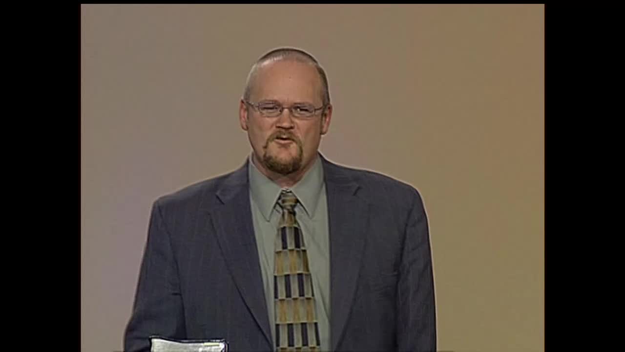 A man in a suit and tie, wearing glasses, speaks directly into the camera. He's on a set, likely for a broadcast on the 3ABN Proclaim! Network in the United States.
