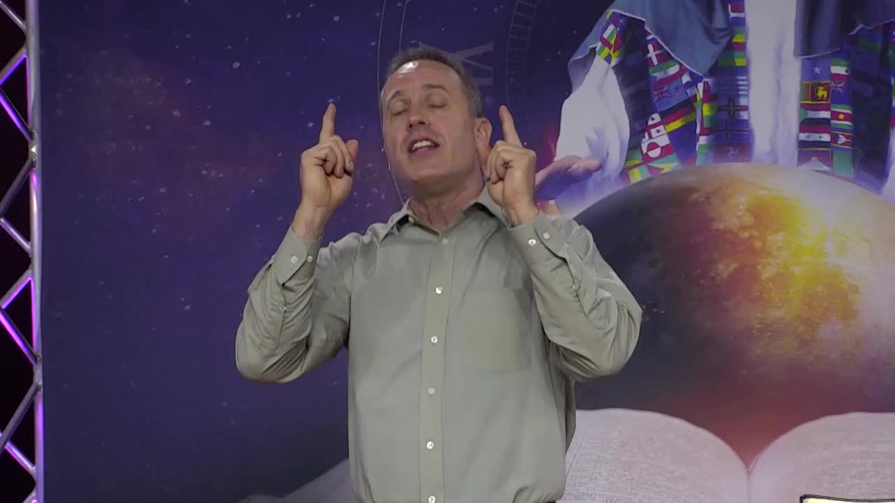 A man in a button-down shirt stands front and center, his eyes lifted as he gestures upward with both index fingers. Behind him, a backdrop featuring a globe and a colorful robe suggests this is a broadcast from the 3ABN Proclaim! Network in the United States.

