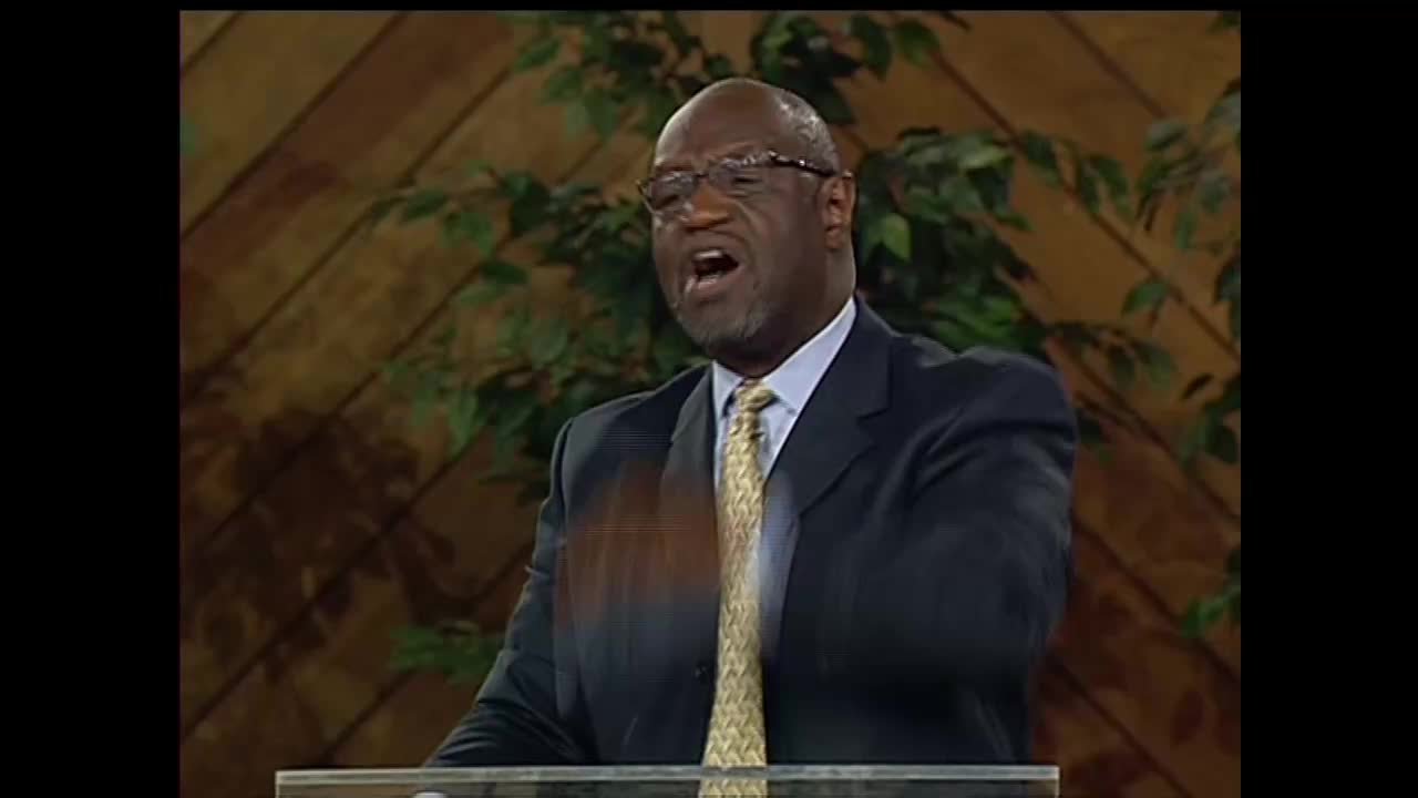 A man in a suit, tie, and glasses is speaking emphatically, his mouth open. His right hand is raised, a blur of motion in front of him.

