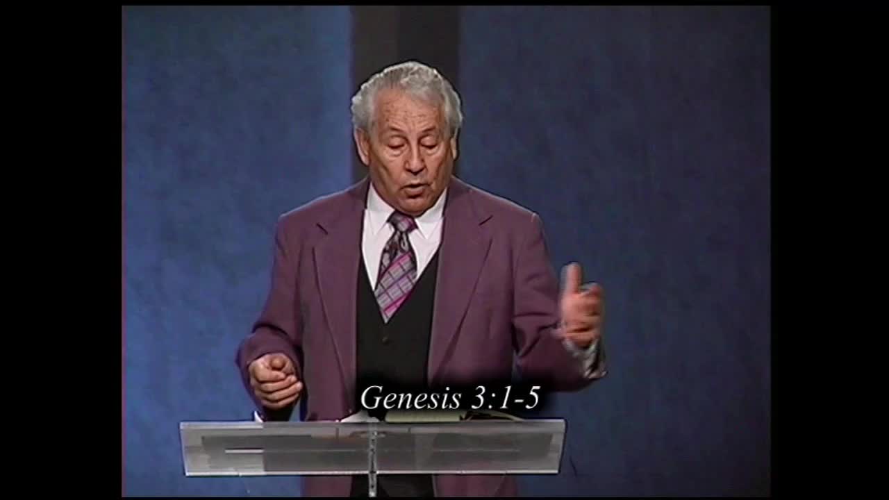 A man in a purple suit stands behind a clear podium, gesturing with his hands as he speaks. Text on the screen reads "Genesis 3:1-5."
