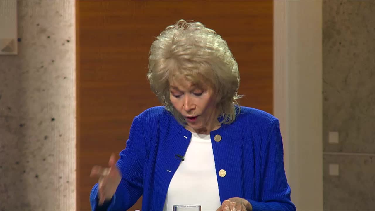 A woman with blonde hair, wearing a bright blue jacket over a white shirt, gestures with her left hand as she speaks. She appears to be on a set for the 3ABN Proclaim! Network, broadcasting from the United States.