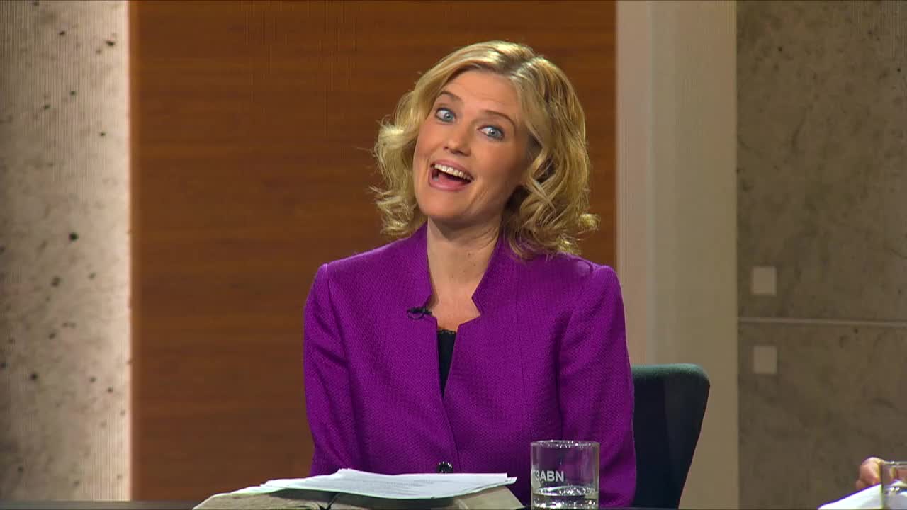 A woman in a vibrant purple jacket speaks animatedly, her blue eyes wide and her mouth open. She's seated at a table with a Bible and a glass bearing the 3ABN Proclaim! Network logo.