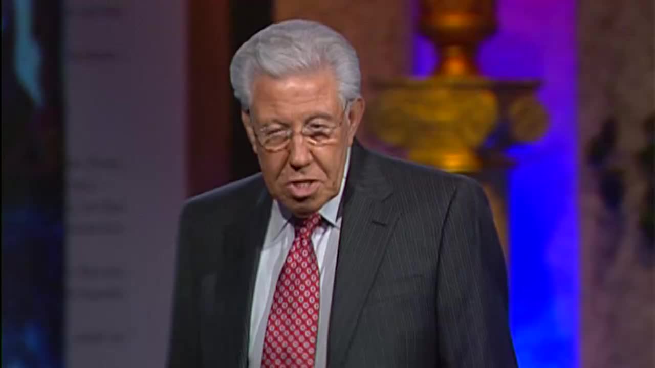 A man in a pinstripe suit and a red patterned tie speaks from a stage, his glasses reflecting the lights. The 3ABN Proclaim! Network logo is visible on a screen behind him.