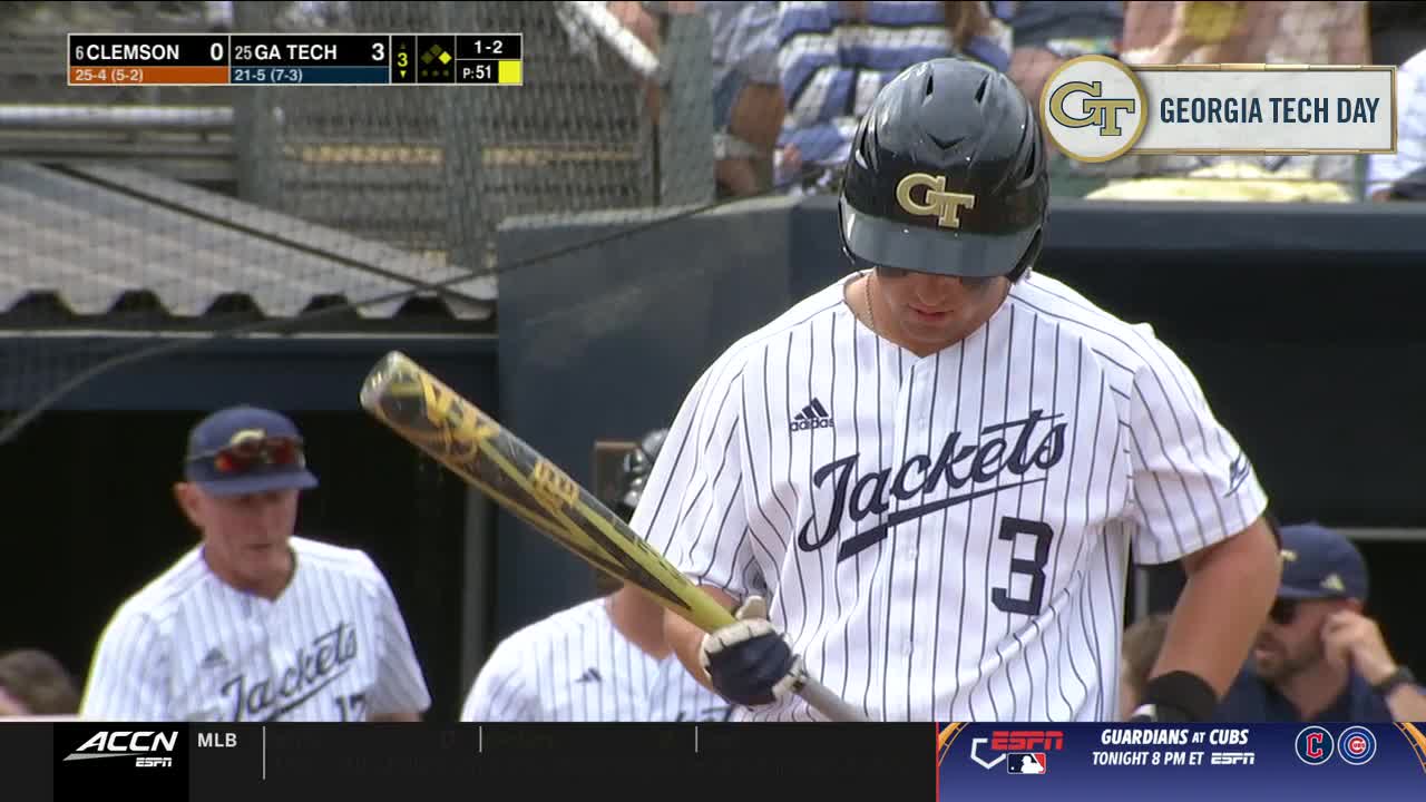 The Georgia Tech batter, in pinstripes and a black helmet, grips his bat, eyes downcast.  The coach, also in a "Jackets" uniform, watches from the dugout.
