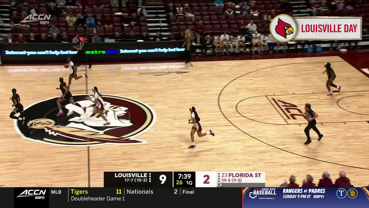The Louisville player with the ball dribbles up the court, pursued by a Florida State defender. The score is close, and the clock shows just over seven minutes left in the first quarter.
