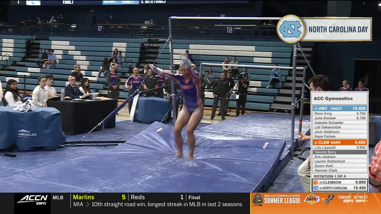 A gymnast in a purple and orange leotard is mid-air, having just dismounted from the uneven bars. The ACC Network is broadcasting the competition, and the score for Clemson is displayed on the screen.
