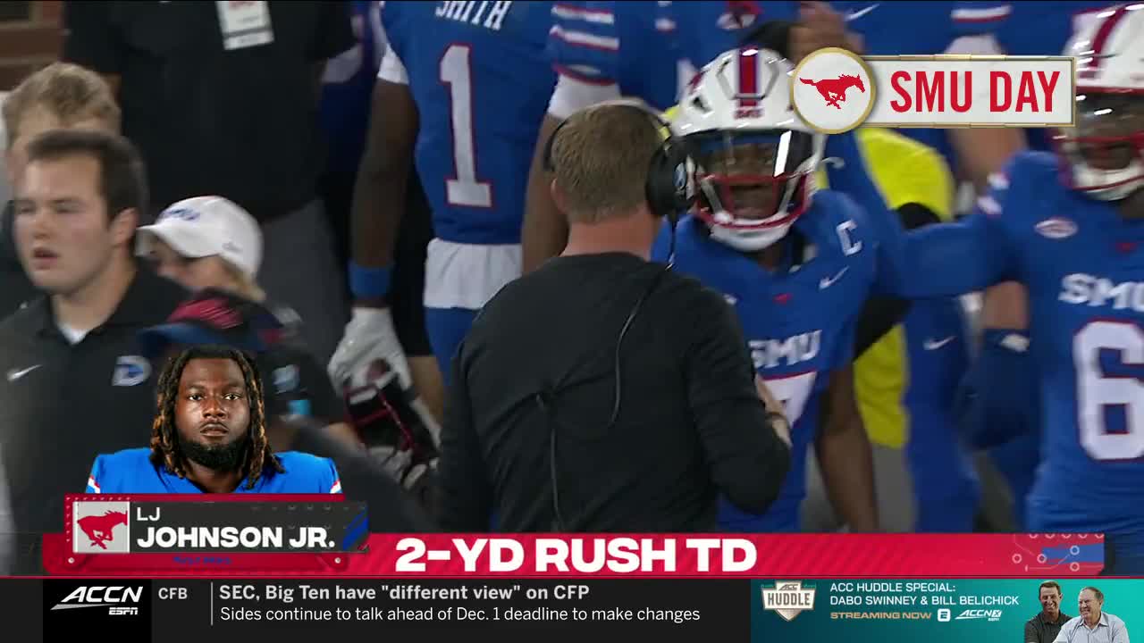 The player in the white helmet and blue jersey is smiling as he walks off the field, while his coach is talking to him. The graphic at the bottom announces a two-yard rushing touchdown.
