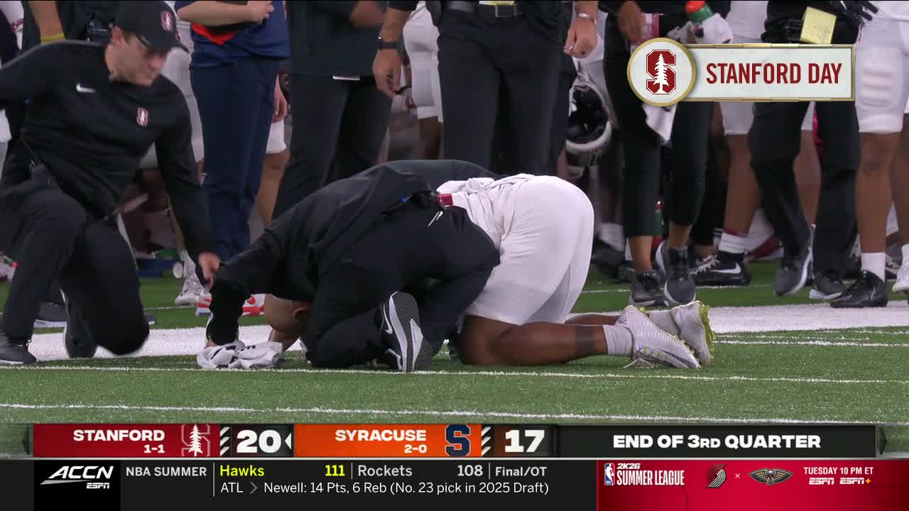 A player is on his knees, head down on the field, and a coach is kneeling beside him. The ACC Network broadcast shows the end of the third quarter of a Stanford versus Syracuse game.
