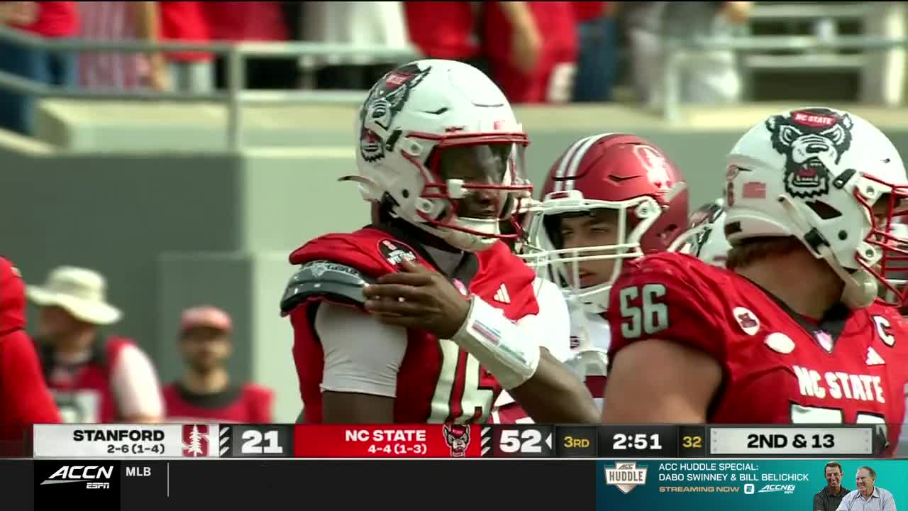 The NC State quarterback, in his white helmet, is looking to his left, perhaps at the play. A teammate, wearing number 56, stands beside him.
