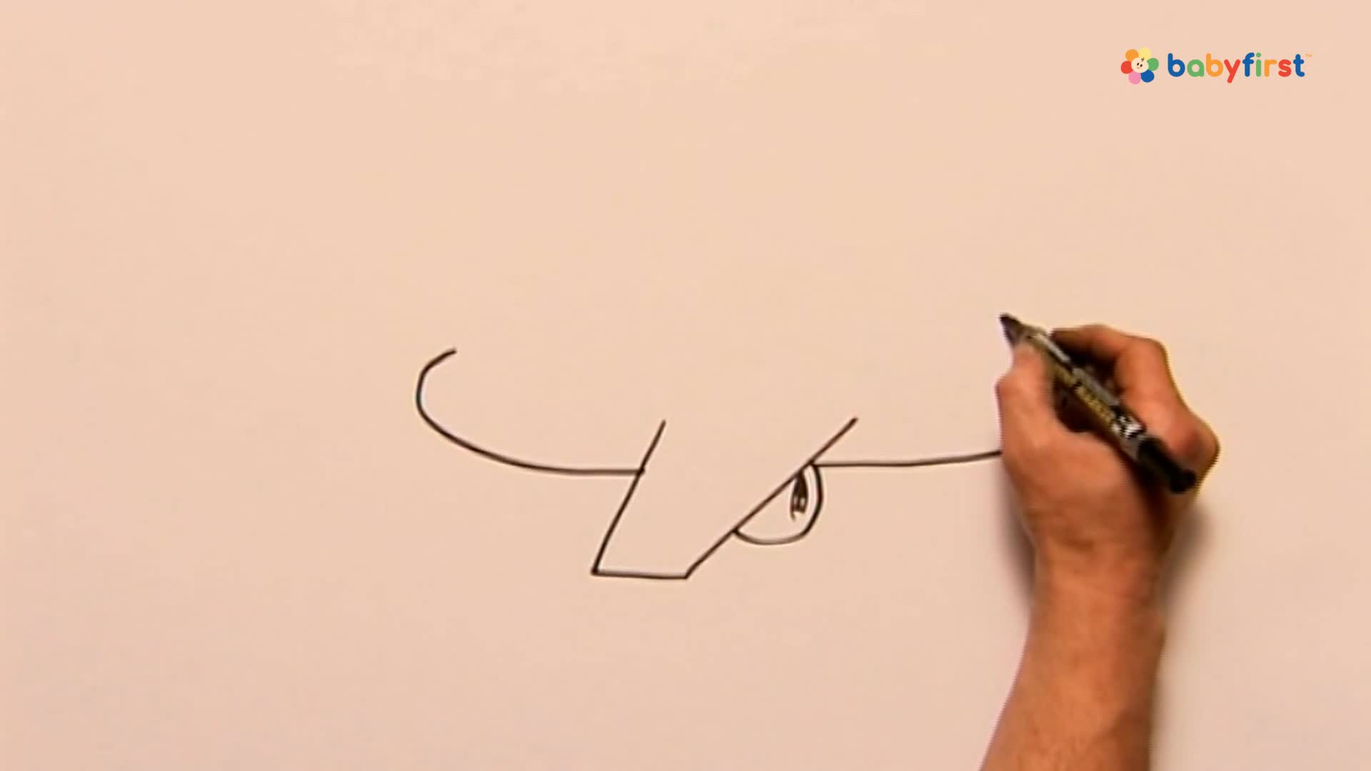 A hand holds a black marker, extending a line to complete the drawing of a cartoon face. The eye is already drawn, and the nose is taking shape.

