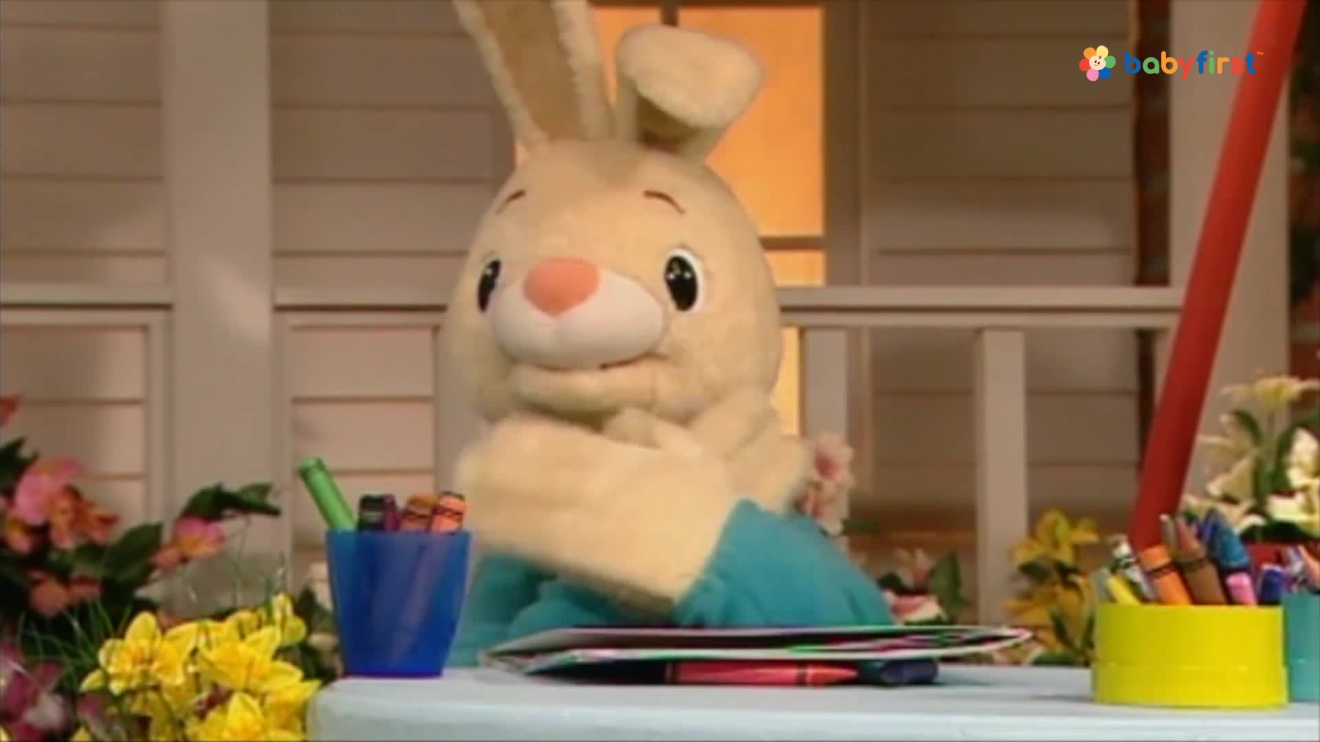 A plush bunny, wearing a blue shirt, sits at a table with crayons and a drawing pad. The bunny seems to be holding the pad, ready to draw.
