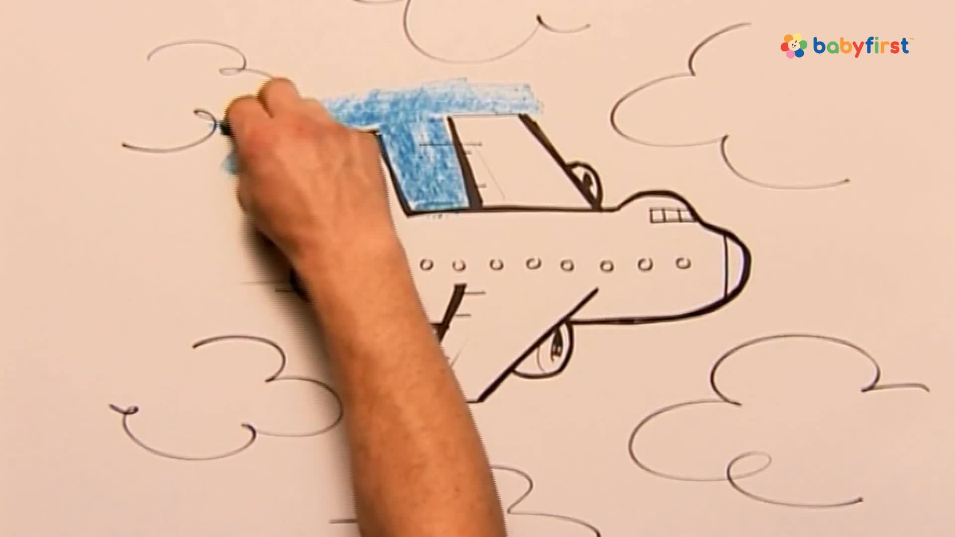 A hand colors the top of a drawn airplane with blue crayon, the color spreading across the white surface. The plane, outlined in black, is surrounded by simple, sketched clouds.
