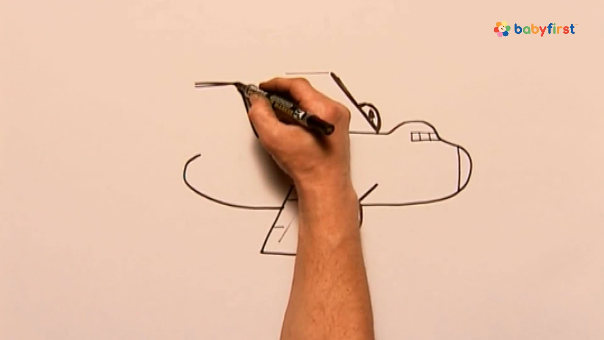 A hand holds a black pen, drawing a line across the top of a cartoon airplane. The pen continues to add details, shaping the plane's wing.
