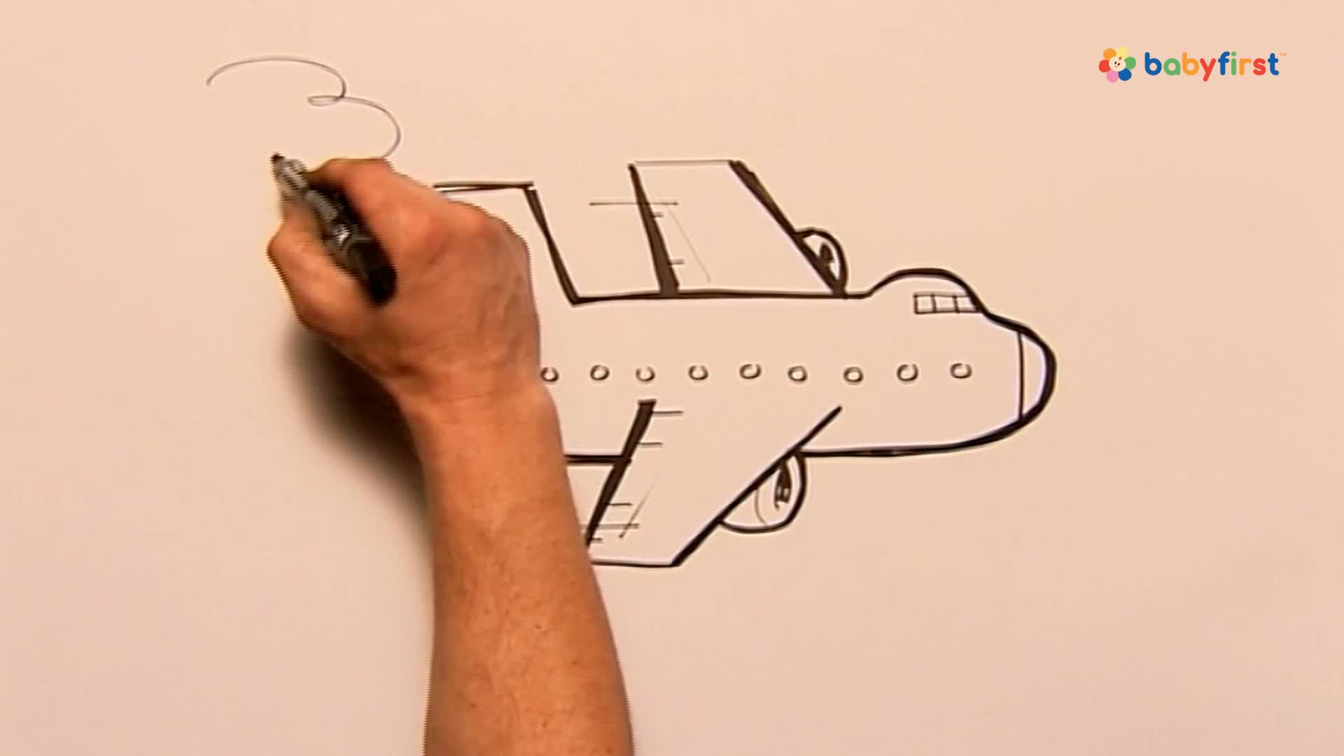 A hand is drawing a cartoon airplane with a black marker. Smoke curls above the plane as it's being outlined on a white surface.
