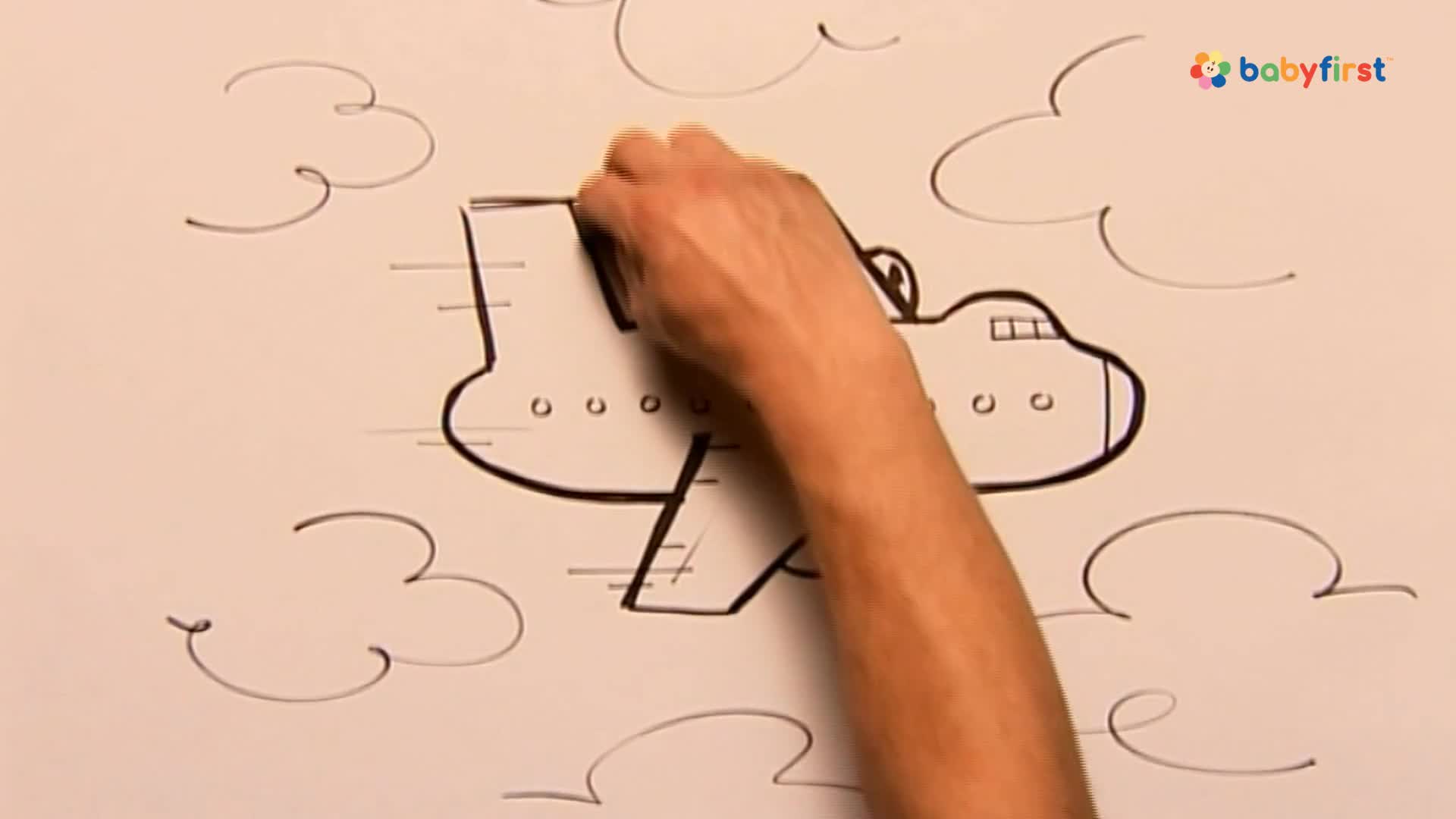 A hand is drawing a cartoon airplane on a white surface, adding the top of the plane's body. Black lines trail behind the aircraft, suggesting movement through the sky, with simple cloud shapes scattered around.

