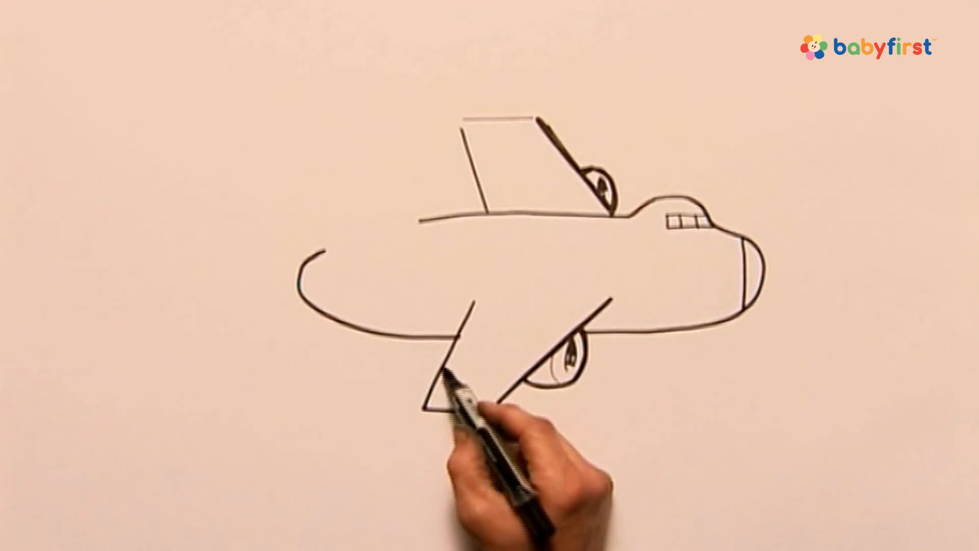 A hand is drawing a simple airplane on a white surface. The plane's wings and tail are taking shape with black lines.
