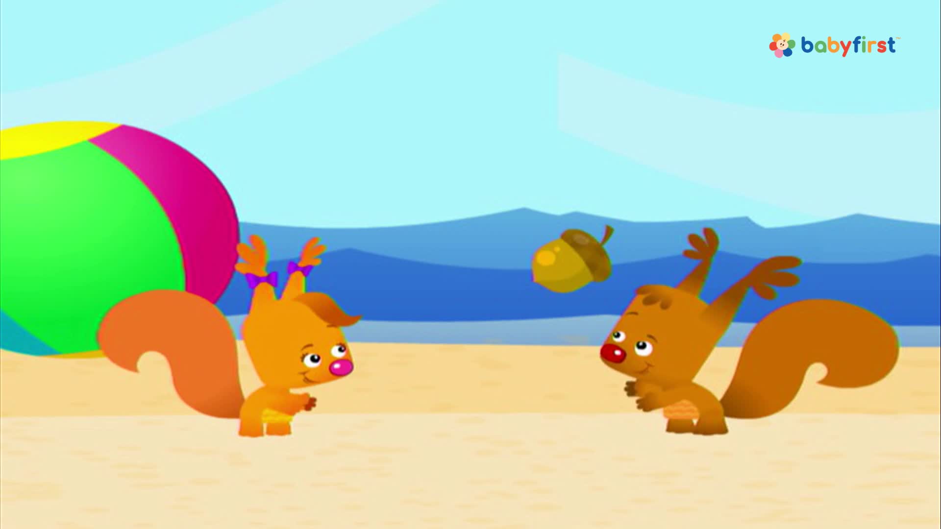 Two cartoon squirrels stand on a beach, looking up at a floating acorn. One has its arms raised, as if ready to catch it.
