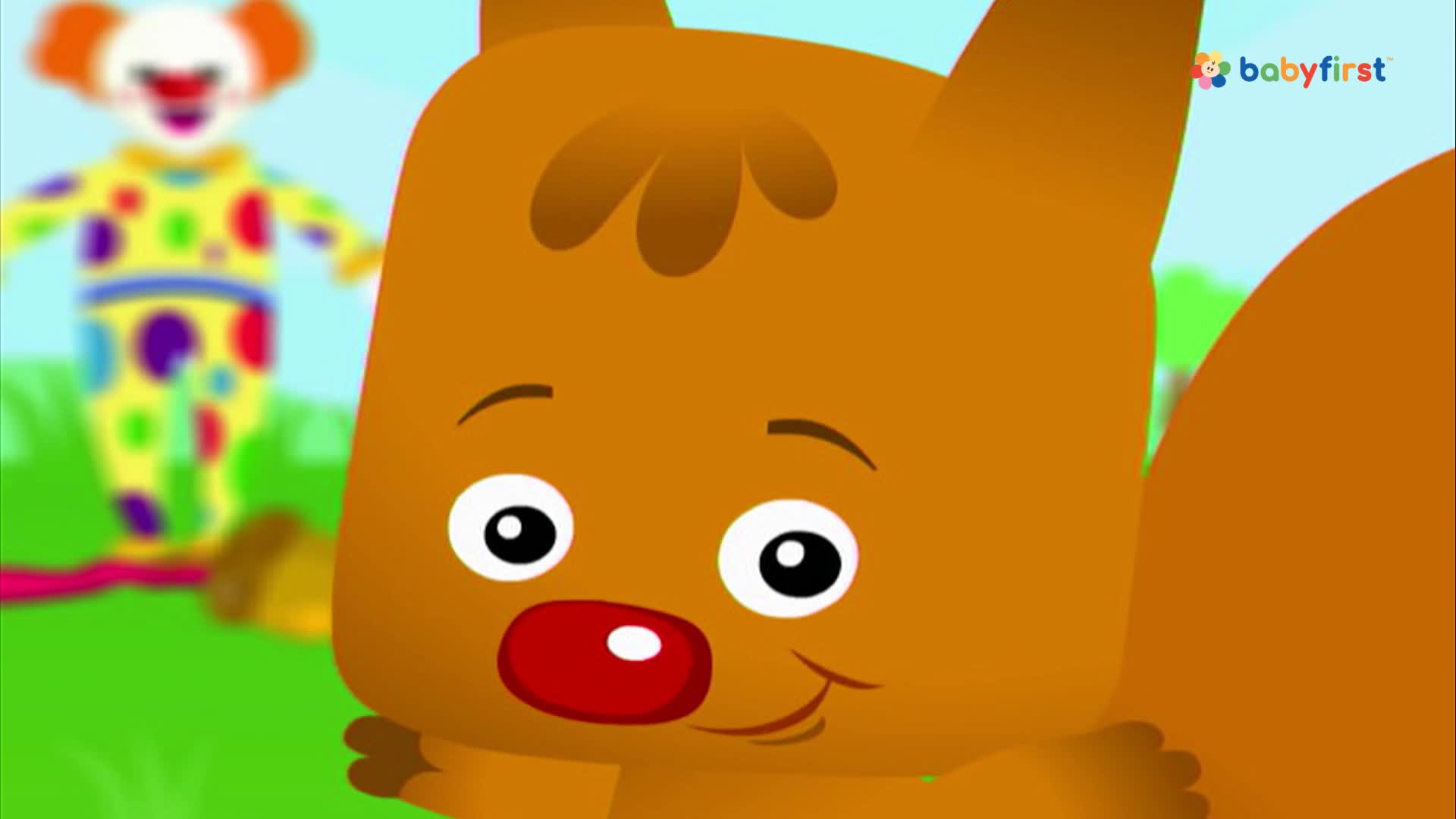 A cartoon squirrel grins, its big eyes fixed on something out of frame. Behind it, a blurry clown in a colorful suit stands on grass.
