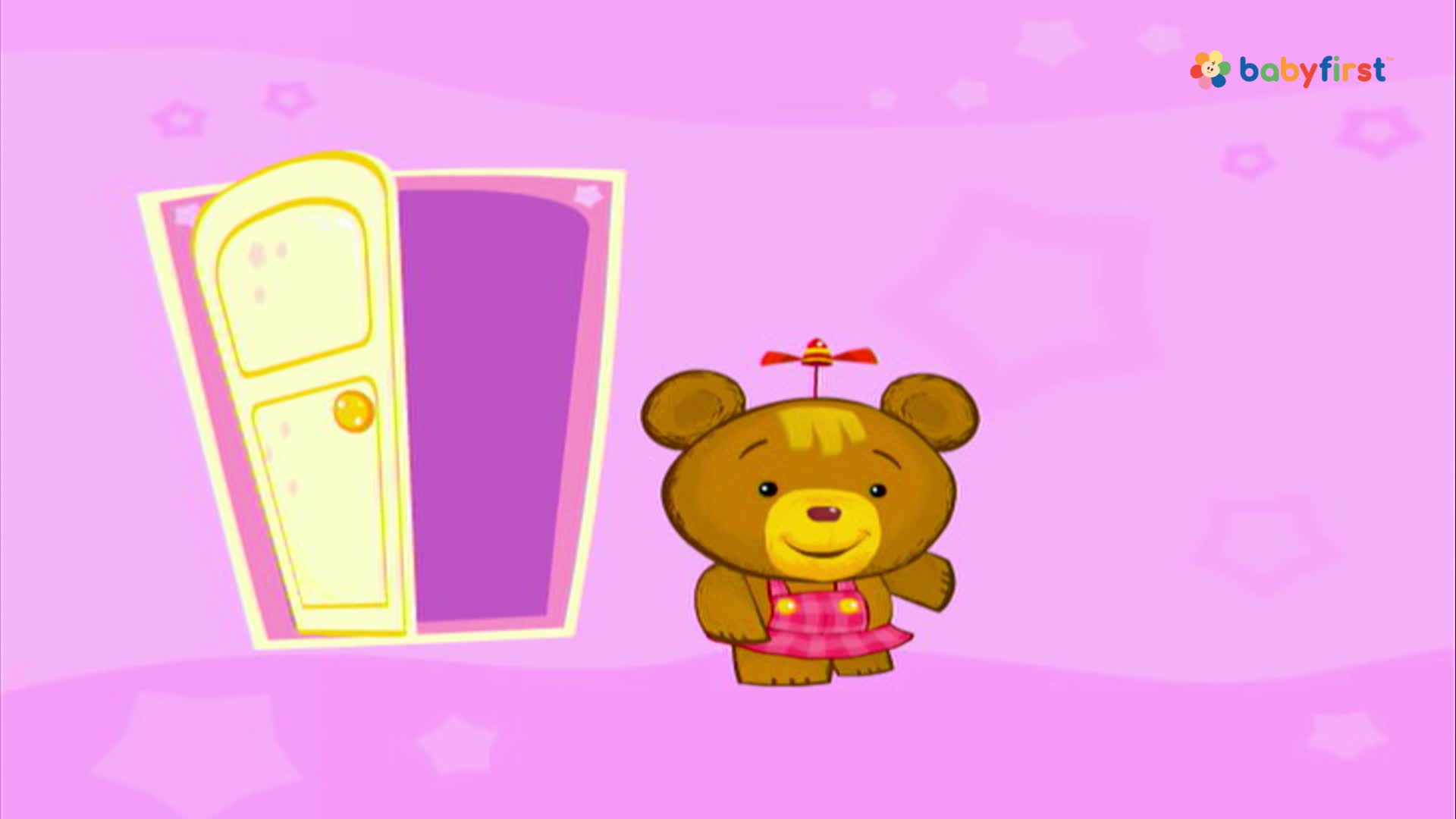 A brown teddy bear with a propeller on its head stands in front of a partially open door. The bear is wearing a pink dress and smiling, as if ready to go through.
