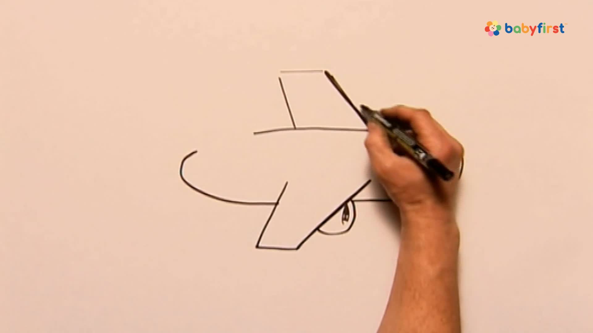 A hand is drawing the tail of an airplane with a black marker on a white surface. The drawing is a simple cartoon style, and the plane's body and wings are already sketched.
