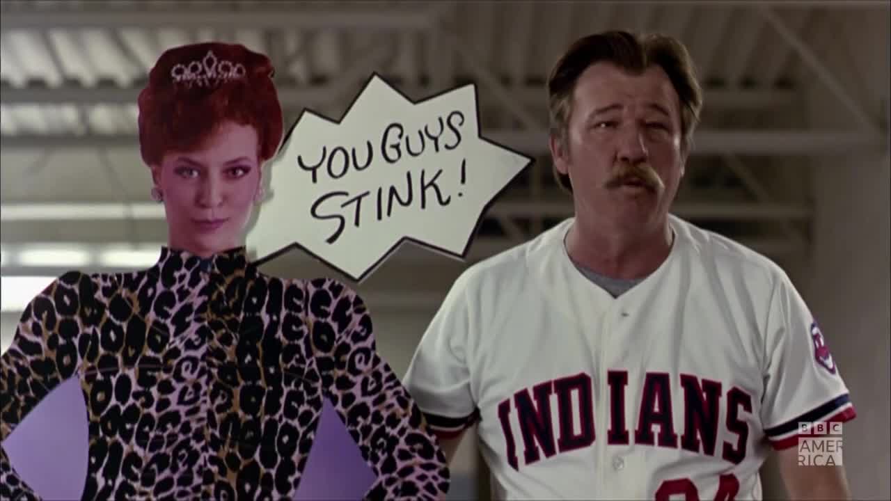 A woman in a leopard-print top and tiara stands next to a man in an Indians baseball jersey. A sign between them reads, "YOU GUYS STINK!"
