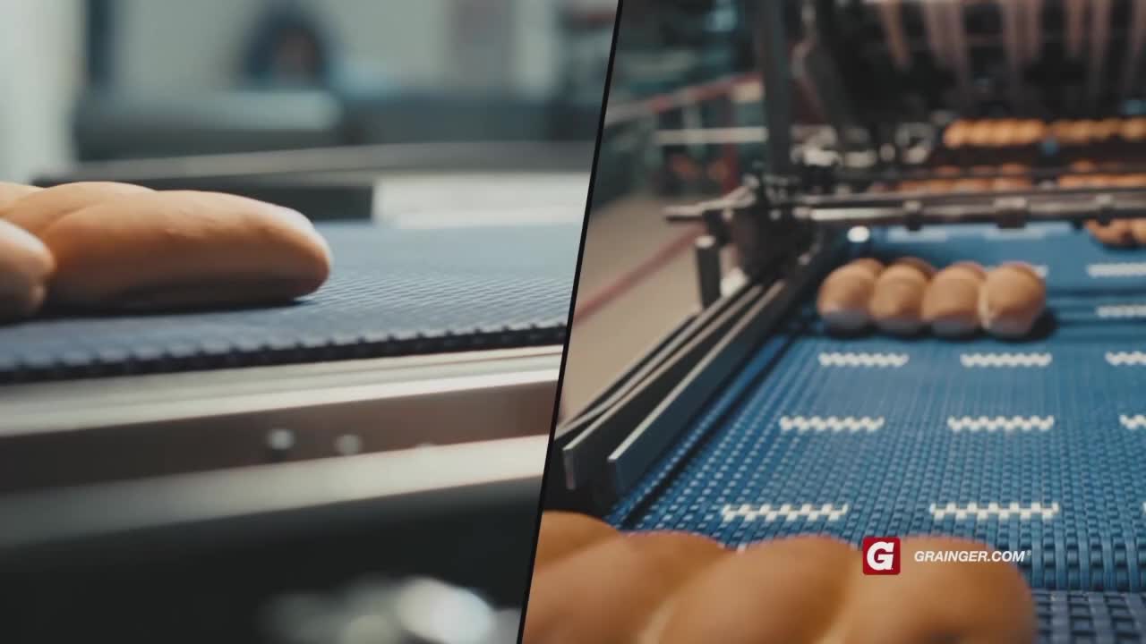 Freshly baked rolls are moving along a conveyor belt. They're heading towards the right, and more are coming.
