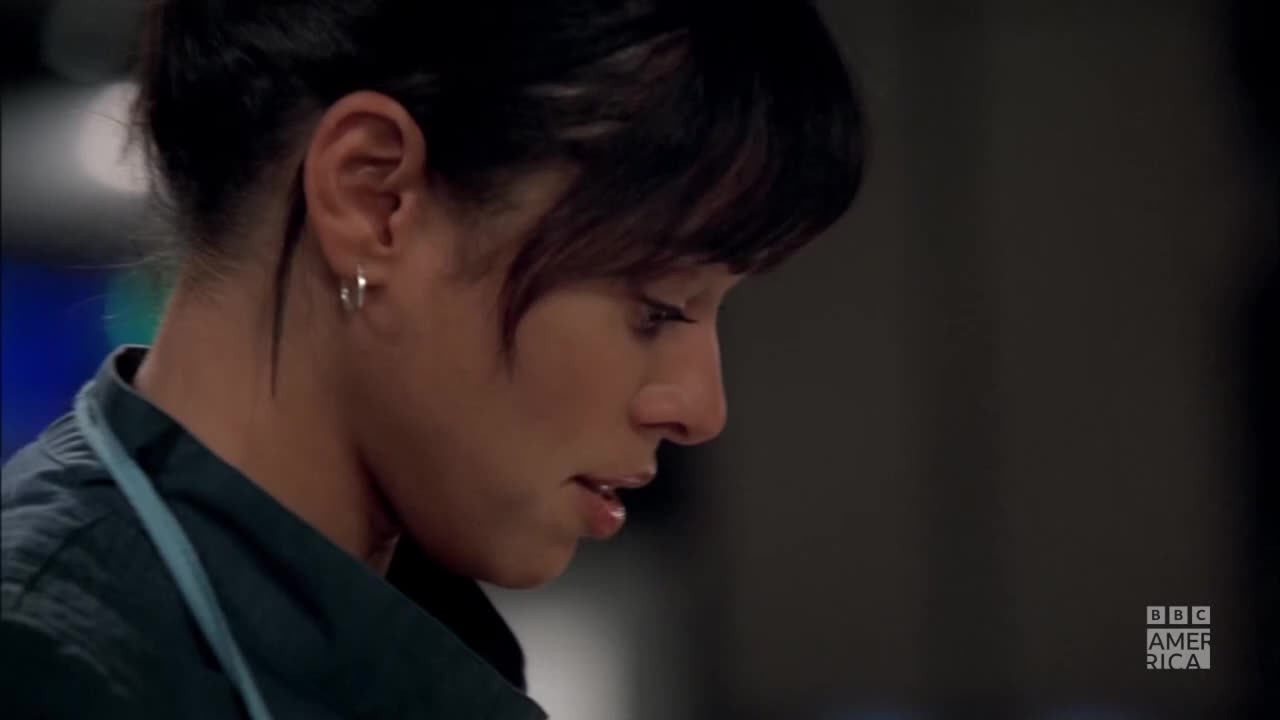 Her gaze is fixed downward, her lips slightly parted as she concentrates on something just out of view. The BBC America logo is visible in the corner.
