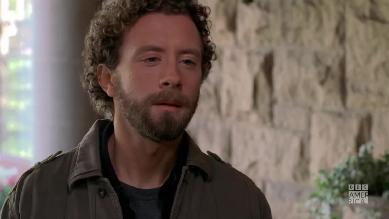 A man with curly hair and a beard looks down, his expression thoughtful. The BBC America logo is visible in the corner, suggesting a scene from a program airing in the United States.
