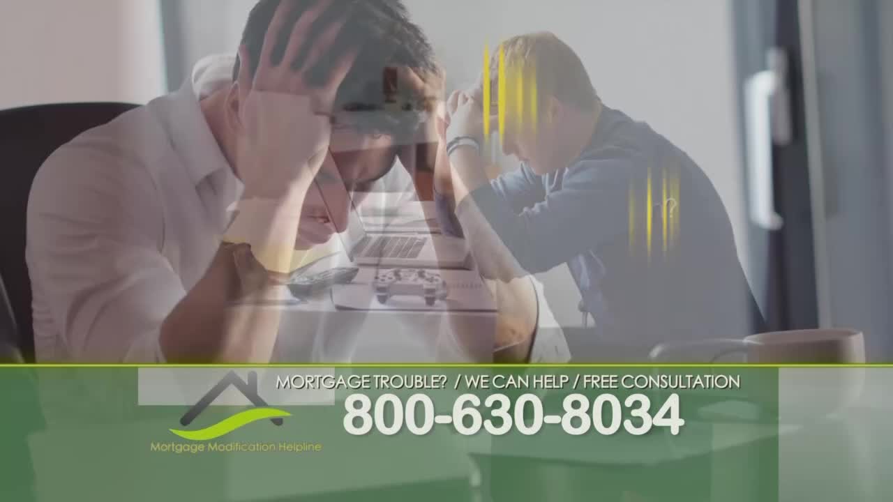 Two men sit at a desk, each with a hand on their head, looking stressed. A phone number for mortgage help is displayed at the bottom of the screen.
