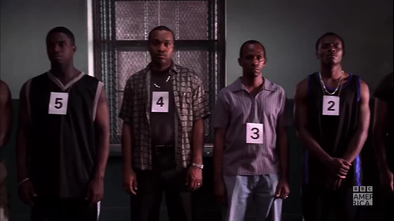 Four men stand in a line, each wearing a numbered placard around their neck. They're in a stark room, and the BBC America logo is visible in the corner.
