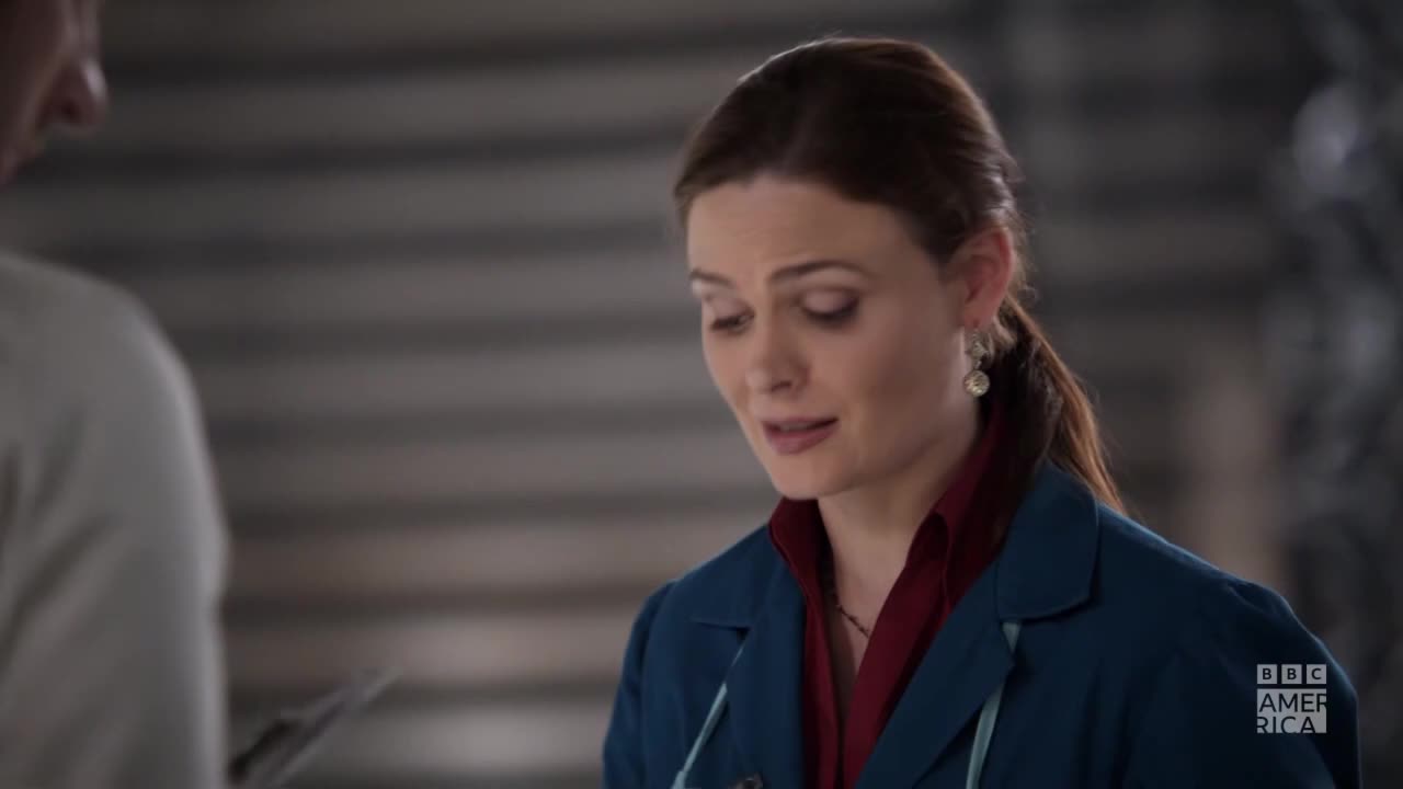 A woman in a teal jacket and maroon shirt looks down, her lips slightly parted as she speaks. The BBC America logo is visible in the corner.
