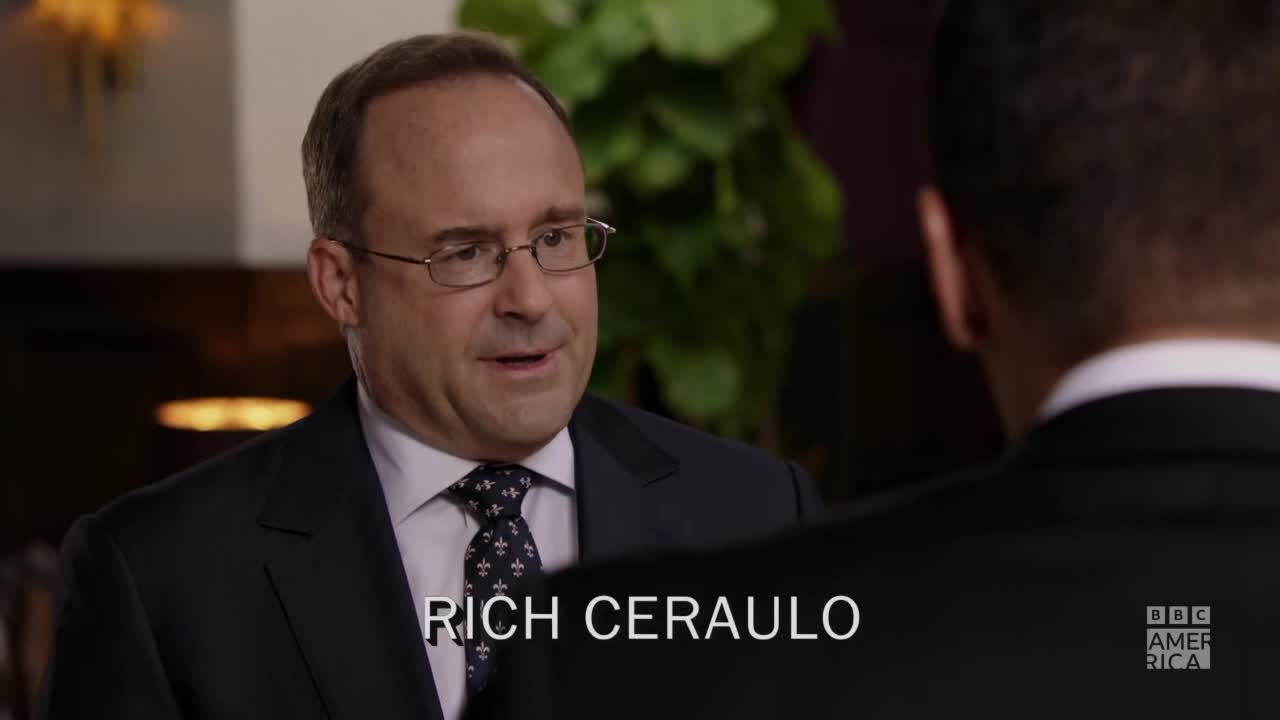 A man in a suit and glasses is speaking, his face lit by soft light. The BBC America logo is in the corner, and the name "Rich Ceraulo" is displayed below.
