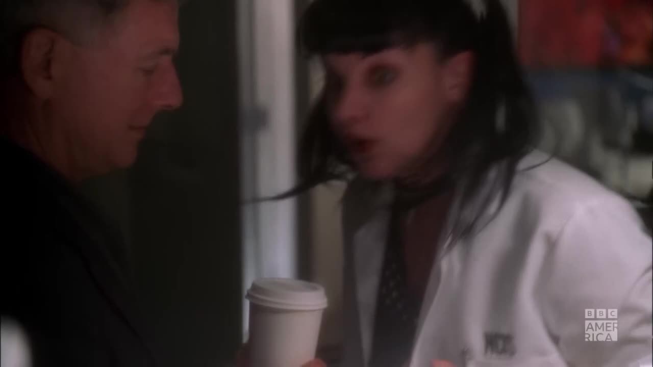 A woman in a white coat gestures animatedly, speaking to a man holding a coffee cup. The BBC America logo is visible in the corner.
