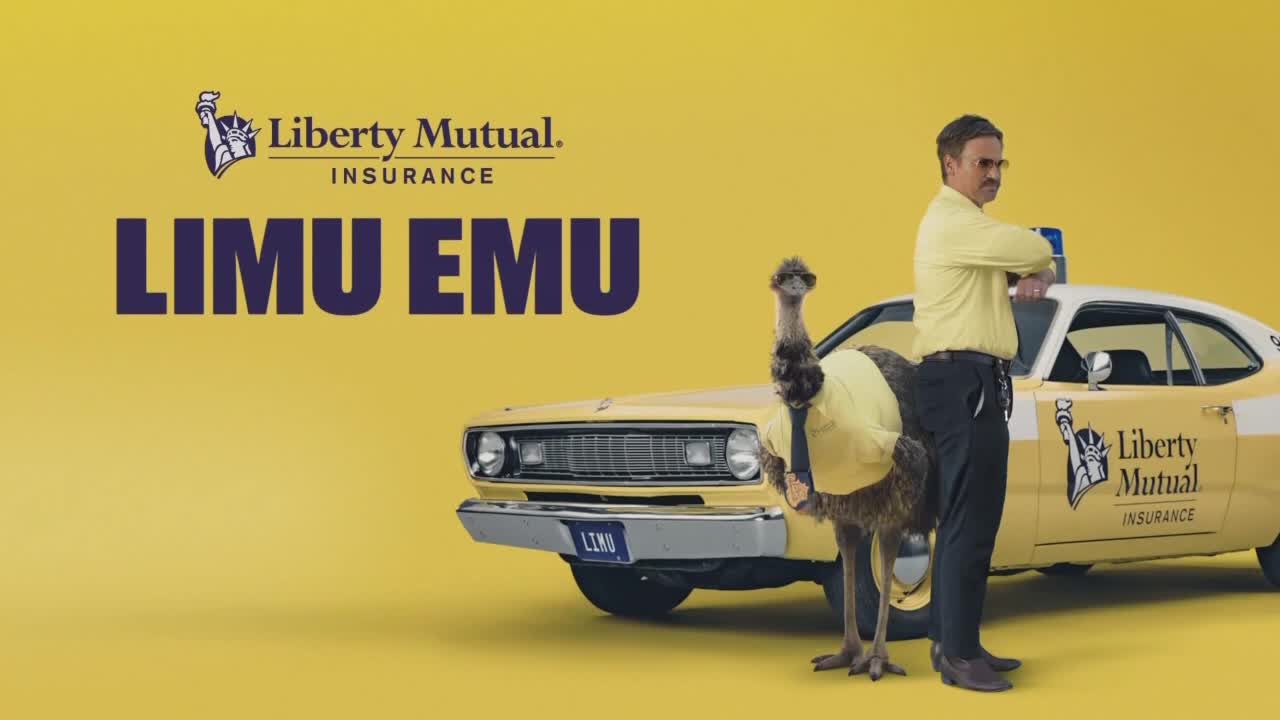 An emu in a yellow shirt stands next to a yellow car, while a man in a matching shirt and dark pants gestures with his arms. The Liberty Mutual Insurance logo is visible on the car and in the background.
