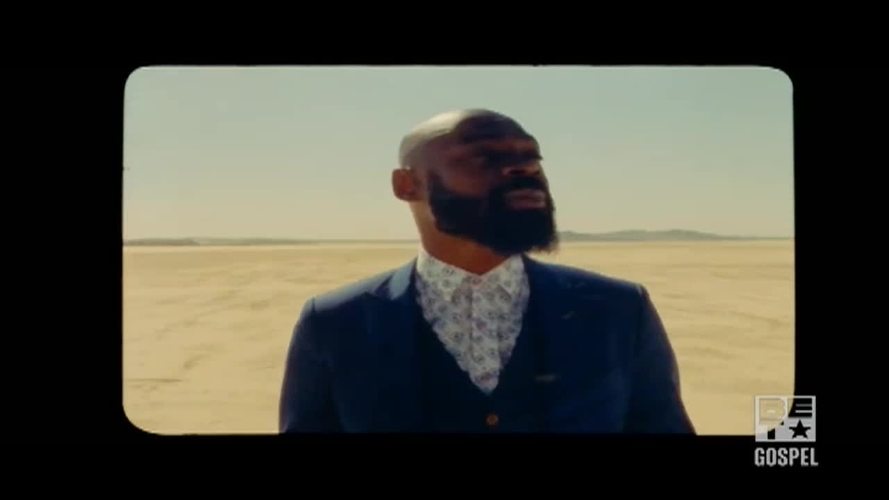 A man in a suit stands in a vast, empty landscape, looking up and to the side. The scene, framed by a vintage-style border, is likely a music video on BET Gospel.
