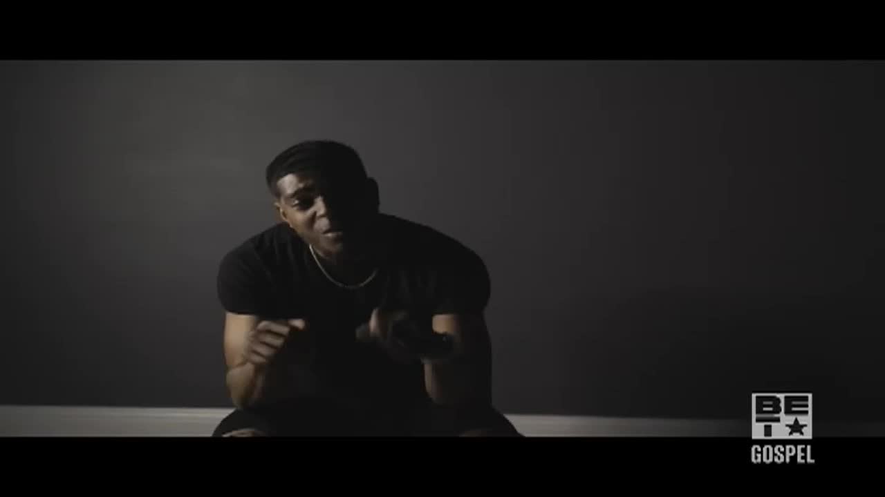 A man in a black t-shirt sits on the floor, lit by a single spotlight. He gestures with his hands as he speaks, a BET Gospel logo visible in the corner.
