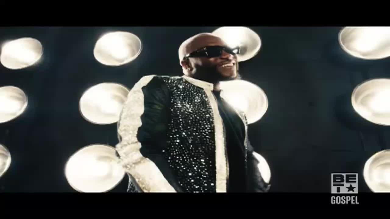 The singer, in a sparkling jacket and shades, beams under the bright stage lights. The BET Gospel logo is visible in the corner.
