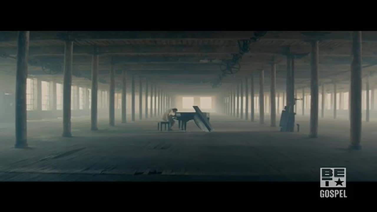 A lone figure sits at a grand piano in a vast, empty warehouse. The music is the only thing moving, echoing through the space, a scene from BET Gospel.
